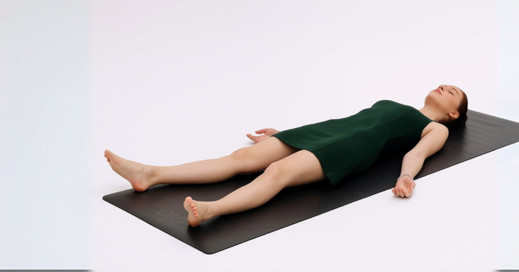 Young woman in a dark green dress practicing Savasana on a mat in a minimalist room – ideal for beginners