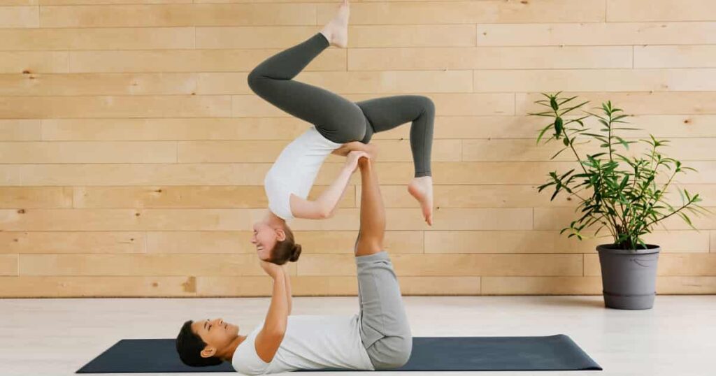 The woman is gracefully balanced upside down on her partner's feet, both maintaining focus and calm expressions—representing trust, sacred connection, and harmony in Tantra Yoga.