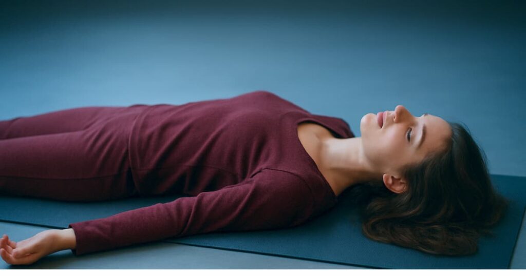A woman achieving deep relaxation in Corpse Pose (Savasana) at the end of a practice, fully releasing stress and calming the nervous system.