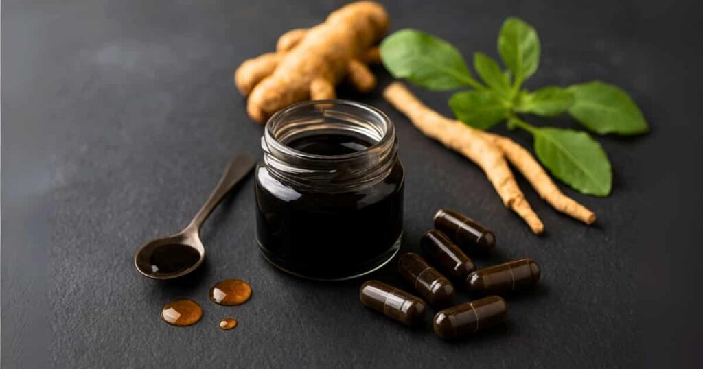 Shilajit benefits shown with resin in a glass jar, capsules, and powder on natural slate background with Ayurvedic herbs.
