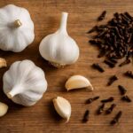 Fresh garlic bulbs and clearly visible dried clove buds on a rustic wooden surface, styled naturally for health and immunity remedies