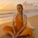 A young woman in a saffron yoga dress practices Butterfly Pose on a beach at sunrise. The golden-hour lighting, ocean backdrop, and serene expression embody Yin Yoga’s calming, beginner-friendly benefits