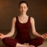 Young woman in dark red yoga dress meditating deeply for better sleep