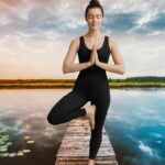 Young woman in a dark dress practicing Hatha Yoga pose peaceful outdoor setting during morning light