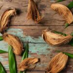 Close-up of dried coconut husk fibers intertwined with green leaves on a weathered wooden surface, symbolizing eco-friendly, spiritual, and practical uses of coconut husks in sustainable living.