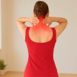 Woman in red dress massaging neck for neck pain relief in a bright room