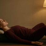 A young woman in dark red loungewear practicing deep relaxation in a supported restorative yoga pose for ultimate stress relief.