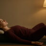 A young woman in dark red loungewear practicing deep relaxation in a supported restorative yoga pose for ultimate stress relief.