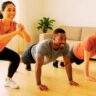 A diverse group of beginners performing easy calisthenics exercises like squats and planks in a living room at home with no equipment.